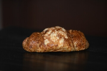 Freshly baked golden croissant resting on a dark wooden surface, showcasing flaky layers and a buttery texture, perfect for breakfast or pastry lovers