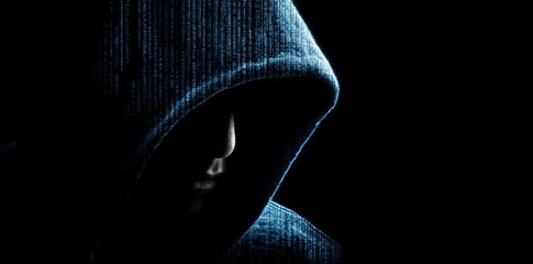 Mysterious hooded figure in dark with digital code overlay representing cybersecurity and hacking.