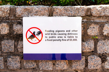 Do not feed pigeons sign white. Signs  Feeding pigeons and other wild birds causind dirtiness public area is liable to a fixed penalty fine of $ 5,000 at Repulse Bay in Hong Kong.