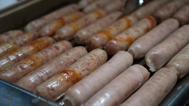 Close up of rows of hot dogs or sausages cooking evenly on roller grill machine.