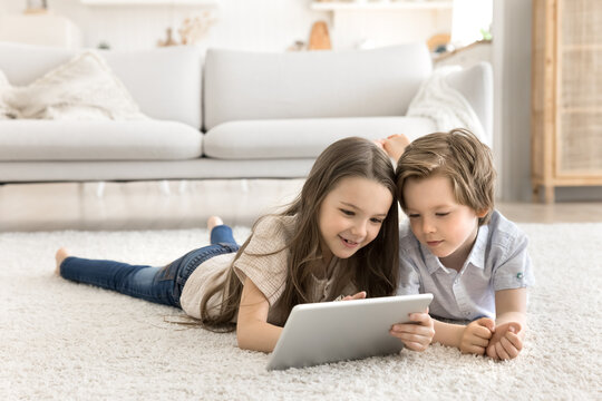 Portrait smiling young children lying on carpet sharing digital tablet