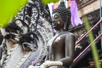 Serene bronze Buddha with gold leaf, jasmine garlands sits peacefully at a Chiang Mai temple....