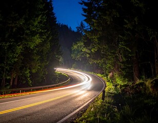 Fototapeta premium Curving road winds through dark woods, car headlights streak in blur under twilight sky