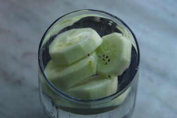 Healthy smoothie with cucumber pieces chopped into it. Health drink with green chopped fruit on a glass.