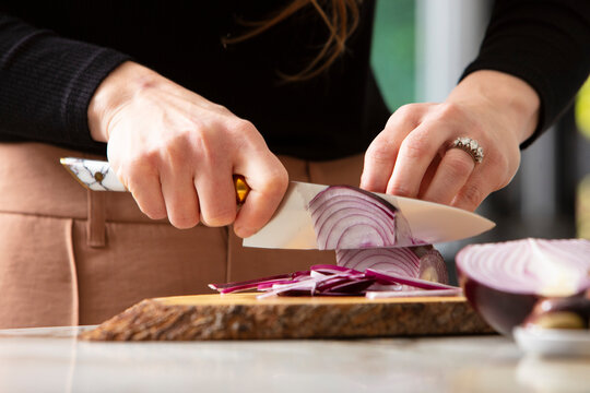 A woman's hands are slicing red onions on a wooden cutting board. 