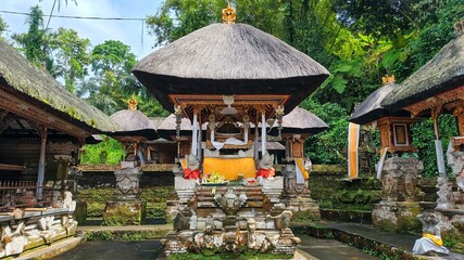 Balinese temple complex with thatched roofs and stone carvings, surrounded by lush greenery.