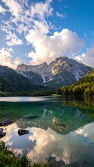 A serene lake mirrors mountains under a partially cloudy blue sky