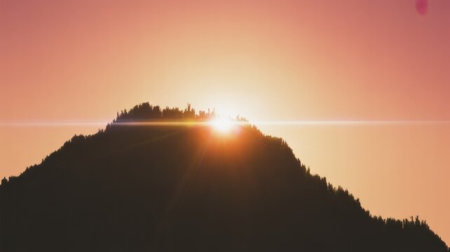 Radiant sunrise or sunset over a silhouetted forested mountain peak, featuring a dramatic lens flare against a warm, gradient sky.