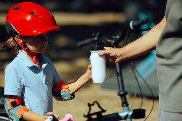 Dad Gives Little Cyclist a Water Bottle to Hydrate. Man helping his daughter to learn how to bike and stay hydrated 

