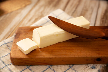 Stick of butter on a cutting board with a wooden knife. A common ingredient in many recipes are used as a spread, it is a high energy food.