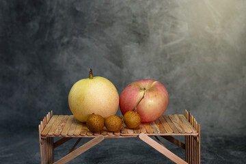 A fresh pear, an apple, and several longan fruits arranged on a wooden surface with a soft dark background, creating a natural and rustic still-life composition that highlights texture and color.