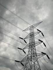 Dramatic Black and White Photo of a High-Voltage Electricity Pylon: Towering Steel Lattice Structure Seen from Below, Holding Power Transmission Lines Against a Moody, Heavily Overcast and Cloudy Sky,