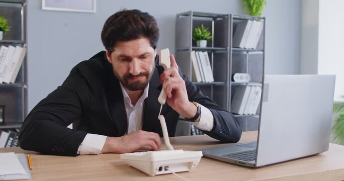 Stress of impatient businessman waiting for important telephone call at workplace in office. Young worried and annoyed corporate employee sitting at desk with laptop to wait landline phone call