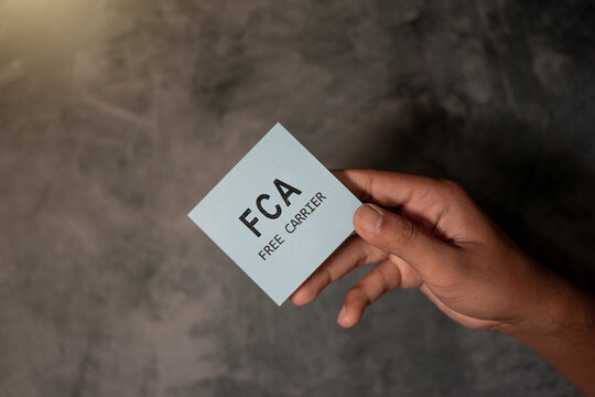 A hand holding a blue card displaying the term &ldquo;FCA &ndash; Free Carrier,&rdquo; representing international trade, shipping terms, logistics, and global commerce on a neutral background.
