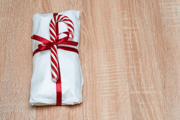 Obraz premium Wrapped gift with candy cane and red ribbon on a wooden surface