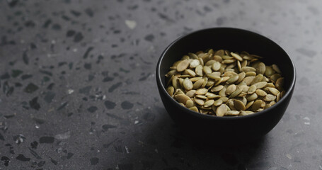 pumpkin seeds in black bowl on terrazzo countertop with copy space