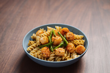 Fusilli pasta with scallops and asparagus in blue bowl on walnut wood surface with copy space