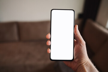Man hold smartphone with white screen in his hand standing indoors in home environment