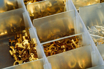 An assortment of gleaming gold-colored crimp terminals and connectors carefully organized in a compartmentalized plastic box for electronics
