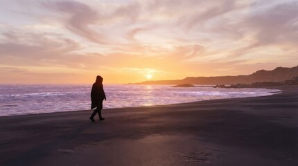 Silhouette of a person walking on a black sand beach at sunset with a beautiful sky.