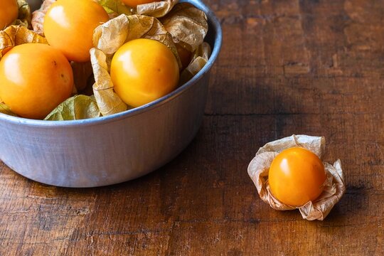 Golden gooseberries in a bowl with one berry on a wooden surface
