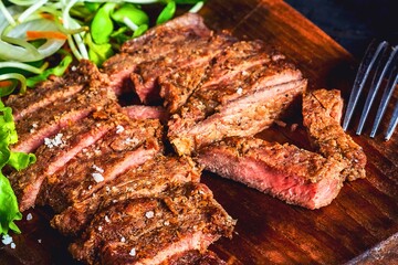 Juicy sliced steak with fresh greens on a wooden board