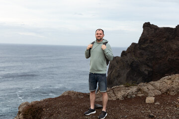 Man standing on rocky coastline with ocean view and cloudy sky in the background