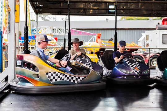 Middle aged man riding on dodgem cars show ride at event with teen son having fun together