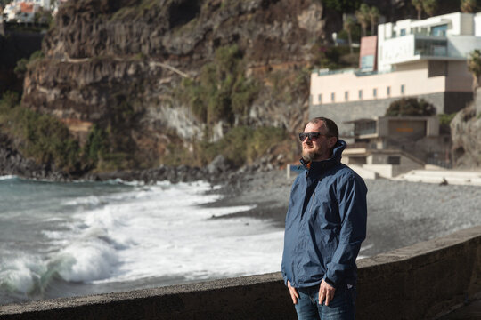 Man standing by the ocean, gazing into the distance, reflecting on life while waves crash against the rocky shore, capturing a moment of solitude - Powered by Adobe