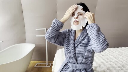 Mature beautiful brunette woman applying a moisturizing sheet face mask at home. Anti-aging skincare routine, beauty self-care, facial treatment, wellness and relaxation concept