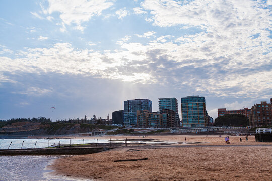 Newcastle Beach with sand, ocean and sunbeams through cloud behind city buildings