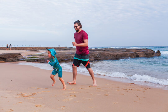Father and young child playing together on the beach runing from waves