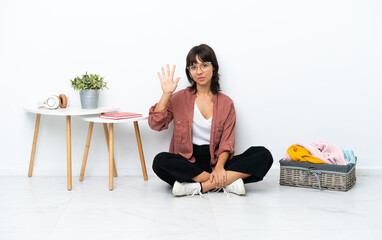 Young mixed race woman folding clothes sitting on the floor isolated on white background counting five with fingers
