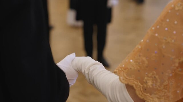 Elegant couple holding hands during a romantic dance at a grand ball. The man wears a black tailcoat and the woman an evening gown