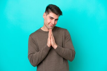 Young caucasian man isolated on blue background keeps palm together. Person asks for something
