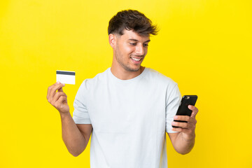 Young caucasian handsome man isolated on yellow background buying with the mobile with a credit card