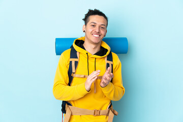 Young mountaineer man with a big backpack over isolated blue background applauding