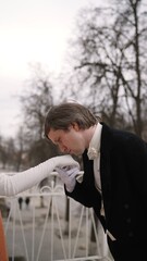 Romantic vintage scene of a man in a tuxedo kissing a woman's gloved hand. Historical reenactment...