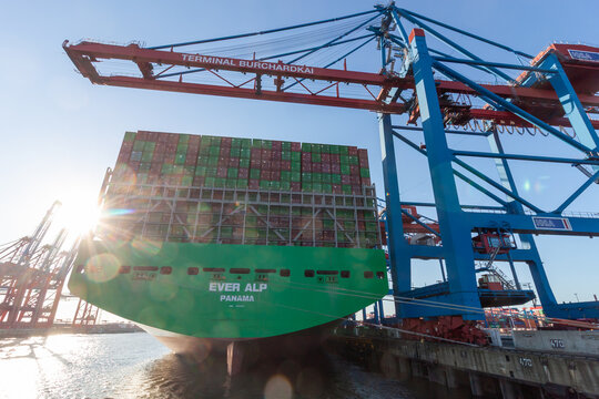 Rear view of the massive container ship Ever Alp docked at Terminal Burchardkai with huge cranes and sun flare