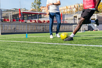 Player trains with coach, kicking soccer ball on bright green artificial turf during sunny outdoor practice session