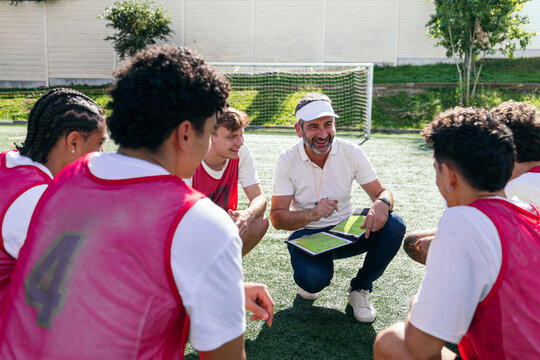 Soccer coach discussing tactics and teamwork with a group of young players during training on a green sports field - Powered by Adobe