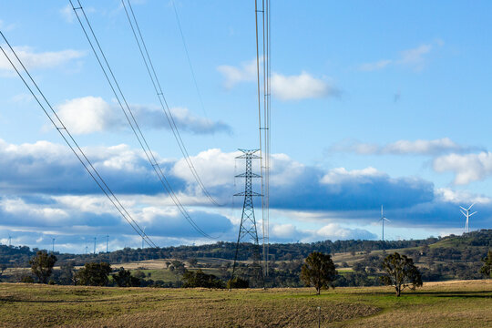 Powerlines and wires of the energy grid with wind turbines on ridgeline in farm land
