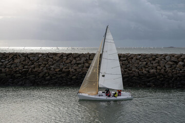 Close-up of a sailing boat entering a harbour, while many sailing boats sail in the distance