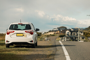 Small car with L Plates displayed parked beside quiet residential road