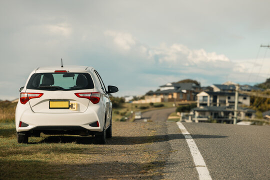 Small car with L Plates displayed parked beside quiet residential road