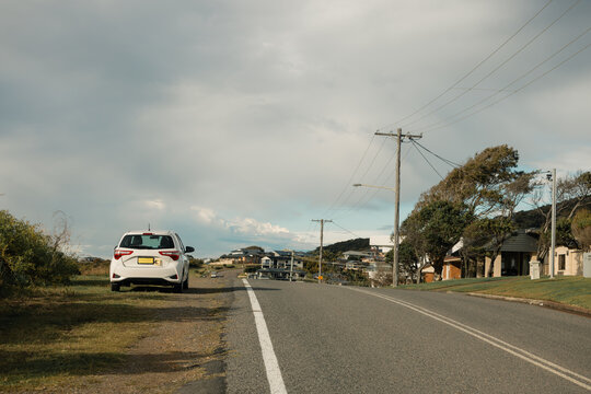 Small white car parked beside residential road with yellow L plates displayed