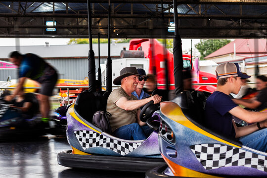 Middle aged man riding on dodgem cars show ride at event with teen son having fun together