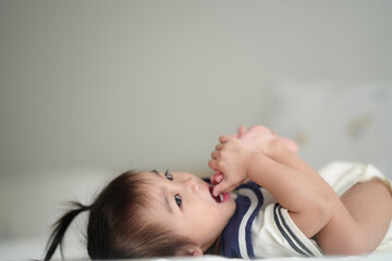 A cute baby lying comfortably on a bed, playfully holding and biting their toes in a bright and soft natural light.