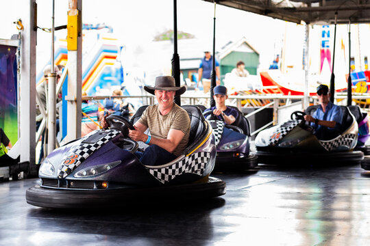 Middle aged man riding on dodgem cars show ride at event with teen son having fun together