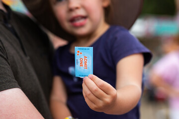 Young child holding admit one ticket for shop carnival ride at event